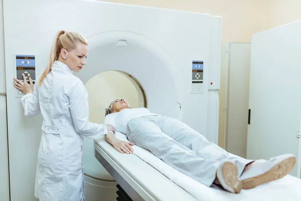 Female doctor starting CT scan procedure of senior patient at medical clinic.
