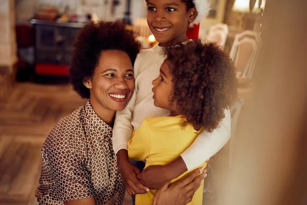 Happy black mother embracing her kids while spending Christmas together at home.