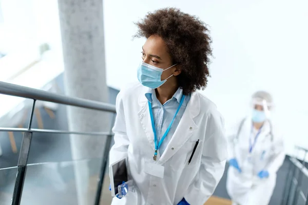 Black female doctor wearing protective face mask while walking through hospital hallway.
