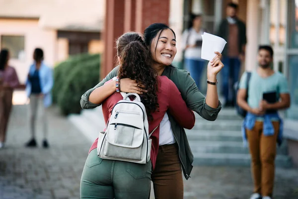 Happy Asian Student Holding Exam Paper Embracing Her Friend While — Fotografia de Stock