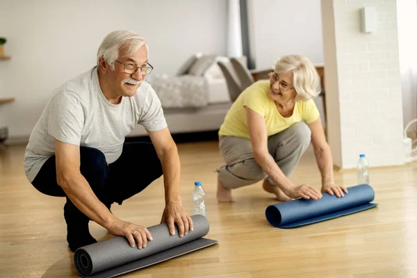 Happy senior couple rolling up their exercise mats after sports training at home.