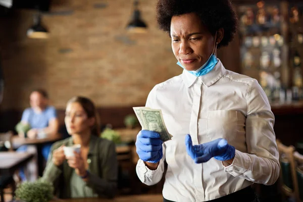African American waitress feeling disappointed with small tip from a customer while working in a cafe during coronavirus epidemic.