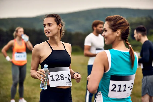 Group of athletes relaxing in nature before the marathon race. Focus is on athletic woman holding a water bottle.