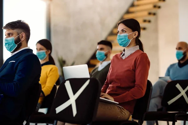 Businesswoman wearing attending an educational event and using laptop while wearing protective face mask in board room.