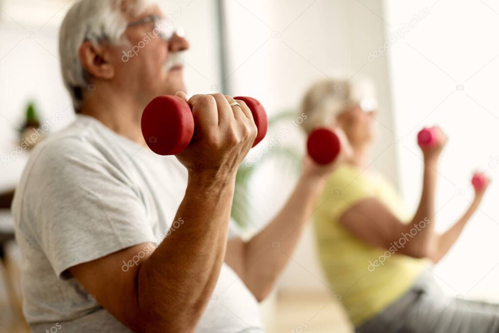 Close-up of senior man and his wife using hands weights while exercising at home. 
