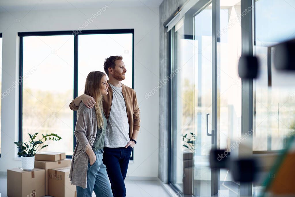 Young happy couple enjoying the view through the window in their new home