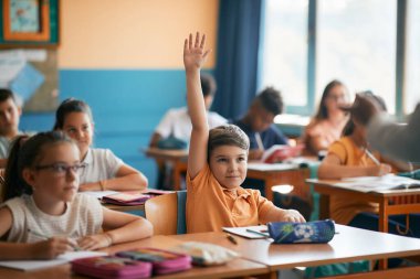 Smiling elementary student raising his hand to answer a question during class at school. 