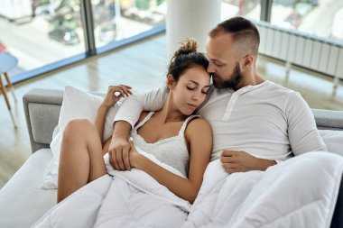 High angle view of affectionate couple lying embraced in the bedroom. 