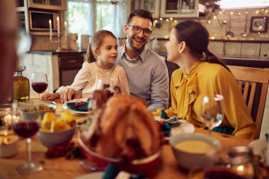 Happy parents and their daughter enjoying during dinner at dining table on Thanksgiving. 