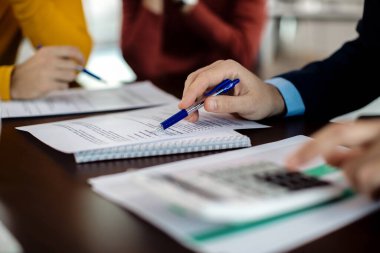 Close-up of insurance agent making calculations while analyzing financial reports of his clients in the office. 