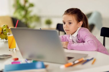 Small girl taking notes while using laptop and e-learning at home. 