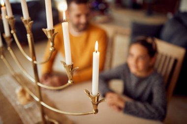 Close-up of burning menorah candles on Hanukkah with father and daughter in the background.