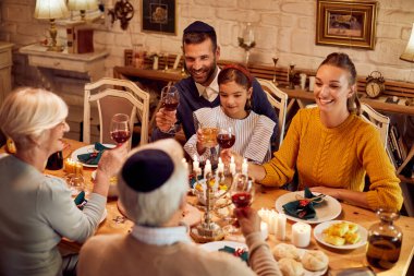 Happy Jewish multi-generation family celebrating Hanukkah and toasting during a meal at dining table.