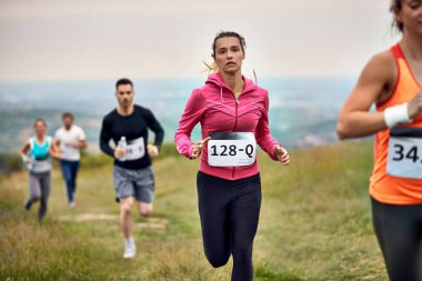 Young athletic woman running while participating in marathon race in nature. 