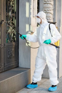Disinfection worker spraying entrance door of public building due to COVID-19 pandemic. 