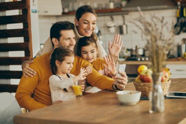 Happy parents with daughters greeting someone during video chat over mobile phone at home.