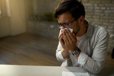 Young businessman feeling sick and blowing nose while working in the office. 