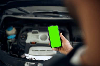 Close-up of auto mechanic using mobile phone while maintaining car engine in a workshop. Copy space.