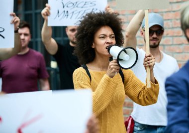 Displeased black woman participating in anti racism demonstrations and shouting through megaphone. 