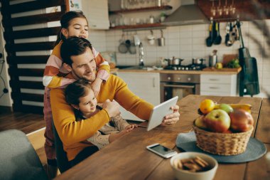 Two little girls and their father using digital tablet while relaxing at home. 