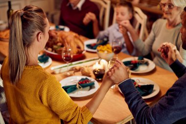 Close-up of multi-generation family saying grace while having Christmas lunch at dining table.