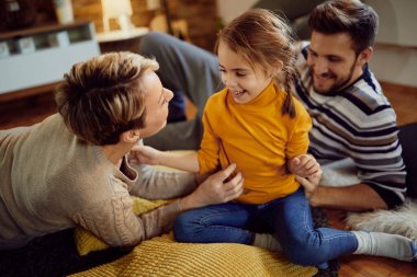 Happy family communicating while relaxing on the floor at home. Focus is on little girl. 