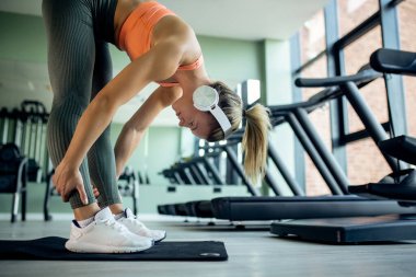 Young sportswoman bending while doing stretching exercises in a gym. 