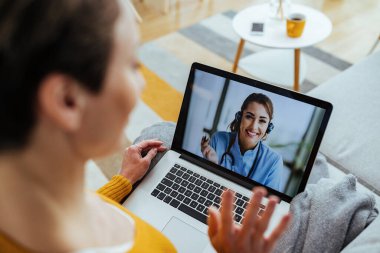 Happy female doctor having video call over a computer with a patient who is sitting at home. 