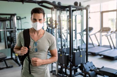 Male athlete wearing protective face mask in a gym during coronavirus epidemic. 