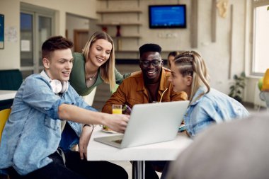 Group of happy university students surfing the net on laptop and having fun in cafeteria. 