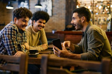 Young happy man showing something funny on cell phone to his friends in a pub. 