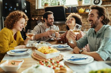 Happy couple toasting with wine and having fun with their friends at dining table. 