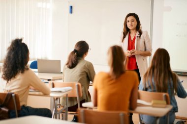 Female professor giving lecture to group of teenagers during a class in high school.
