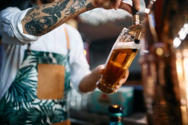 Close-up of barista pouring beer from beer tap while working in a pub. 