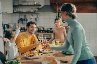Happy man and his wife toasting with wine while having lunch with their small daughter in dining room. 