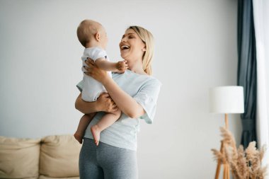 Young happy mother looking at her baby boy while holding him in her arms at home. 