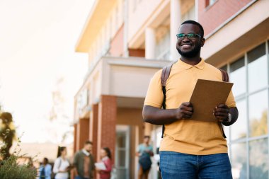 Happy black university student standing at campus and looking away, Copy space.