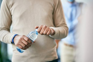 Close-up of black entrepreneur holding water bottle while waiting in line at office building hallway. 
