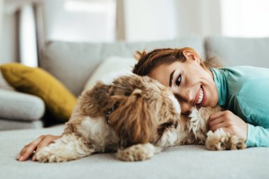 Affectionate woman cuddling her dog while relaxing at home. 