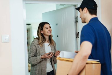 Young happy woman communicating with a courier while receiving home delivery. 
