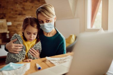 Worried mother and her sick daughter having video call with a doctor from home during coronavirus pandemic. 