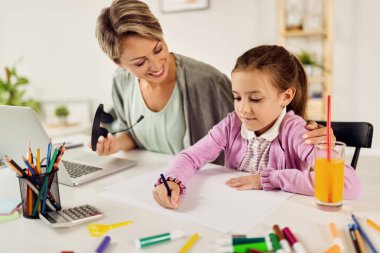 Small girl writing on the paper while learning with her mother at home. 