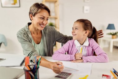 Happy mother and daughter talking while doing homework together. 
