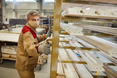 Male carpenter moving rack with processed wood frames while working in a workshop.