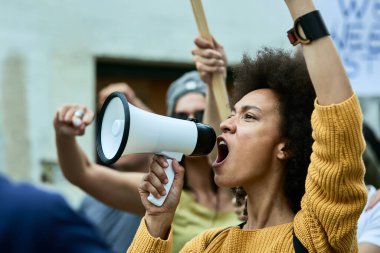Young black woman shouting through megaphone on public demonstrations against racism. 
