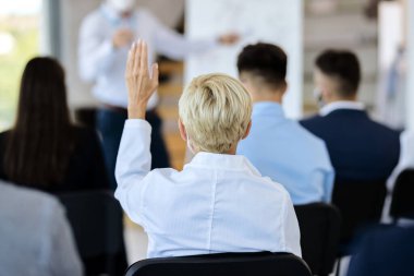back view of businesswoman attending a seminar and raising her arm to ask a question. 