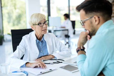 Female doctor going through medical record of a patient while talking to him during an appointment at the clinic. 