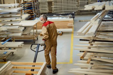 Manual worker pulling pallet jack while working at carpentry warehouse during coronavirus pandemic. 