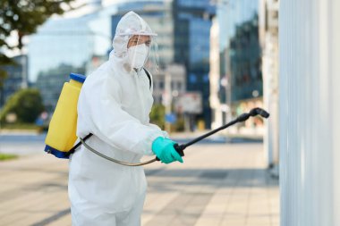 Healthcare worker in protective suit sanitizing city area in order to prevent spread of coronavirus epidemic. 