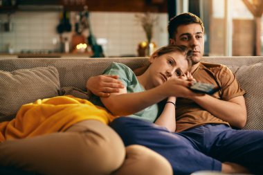 Young woman using remote control and changing channels watching TV with her boyfriend at home. 